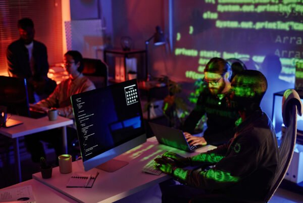 Group of young intercultural office workers sitting by desks in front of computers and decoding data late in the night